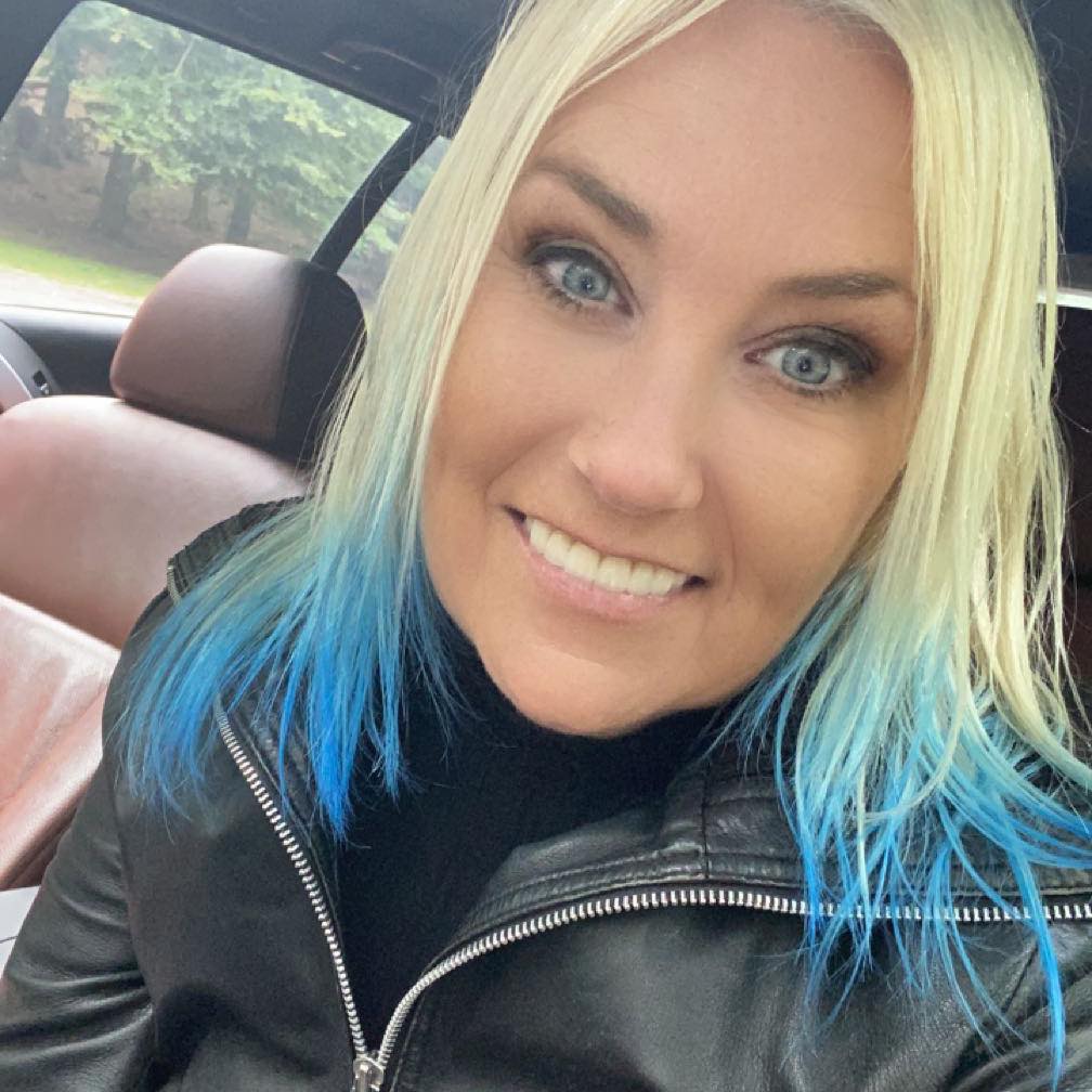 Kvinde med blondt hår og blå spidser smiler i bil